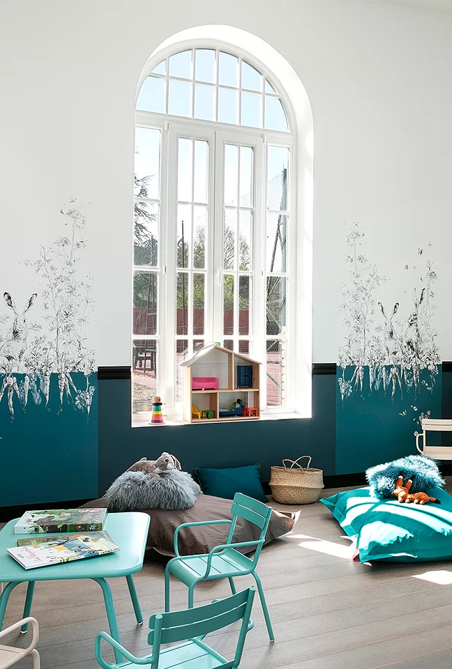 Children's play area with a small turquoise table and wall decorations beneath a large arched window. Les Hauts de Loire – Hotel, Restaurant & Spa – 5-star.
