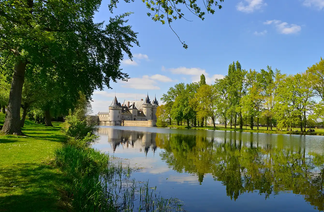 Reflet du Château d'Azay-le-Rideau dans le canal, entouré d'arbres verdoyants et d'un ciel bleu. Votre séjour d'exception aux Hauts de Loire – Hôtel, Restaurant & Spa – 5 étoiles.