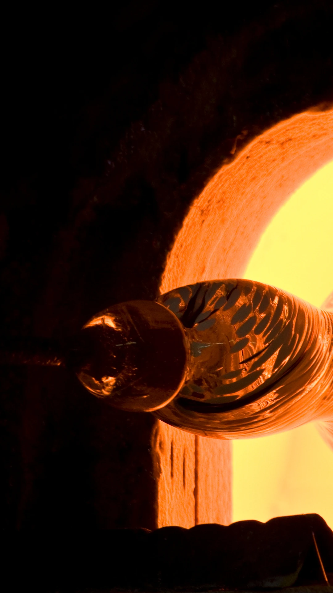 Vue rapprochée : la canne à souffler fait tourner la pièce de verre en fusion contre la chaleur ardente.
