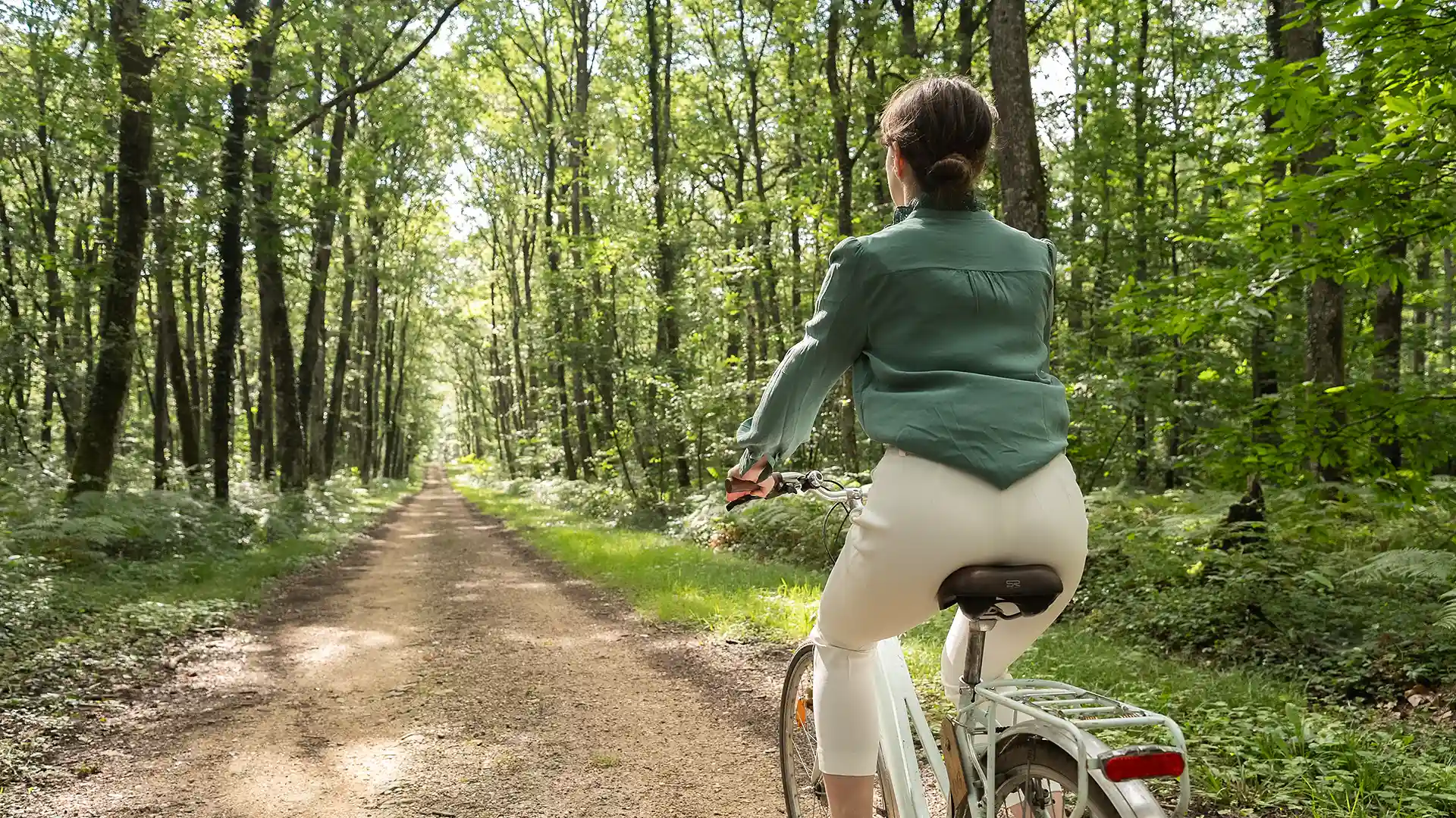 S'éloignant à vélo, cette femme de dos semble explorer les bois avoisinants, un service offert par Les Hauts de Loire – Hôtel, Restaurant & Spa – 5 étoiles.