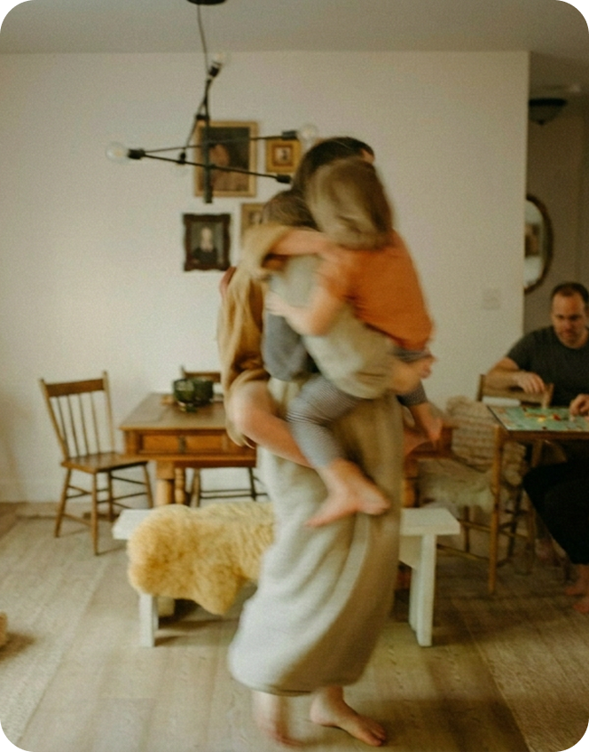 Woman embraces young girl from behind as they both look at a laptop screen on a wooden table.