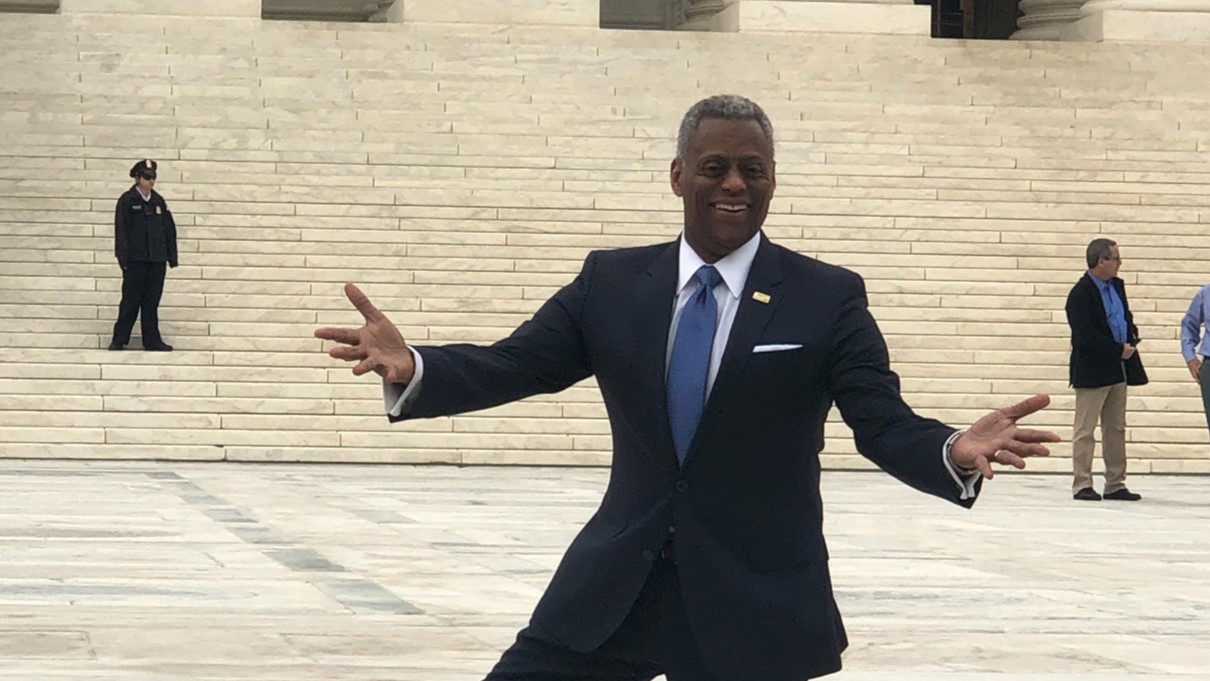 Jesse Milan dressed in a dark suit with blue tie stands on the white marble steps of the U.S. Supreme Cort