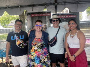 Four people stand arm-in-arm in front of signs that read "Let's Stop HIV Together." 