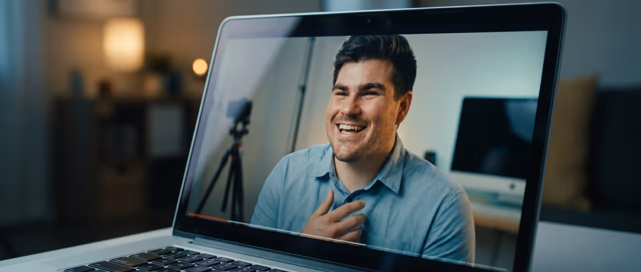 Smiling man in blue shirt on laptop screen during a video call in a home office setting.