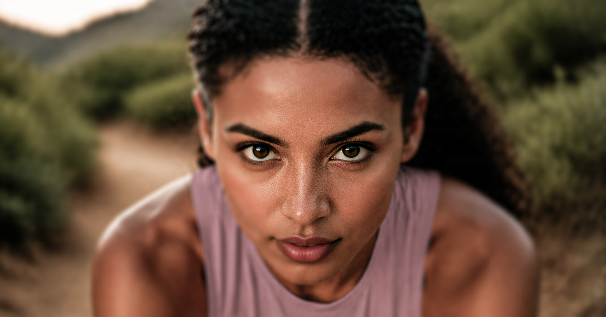 Close-up of a focused woman with braided hair on a nature trail during sunset.