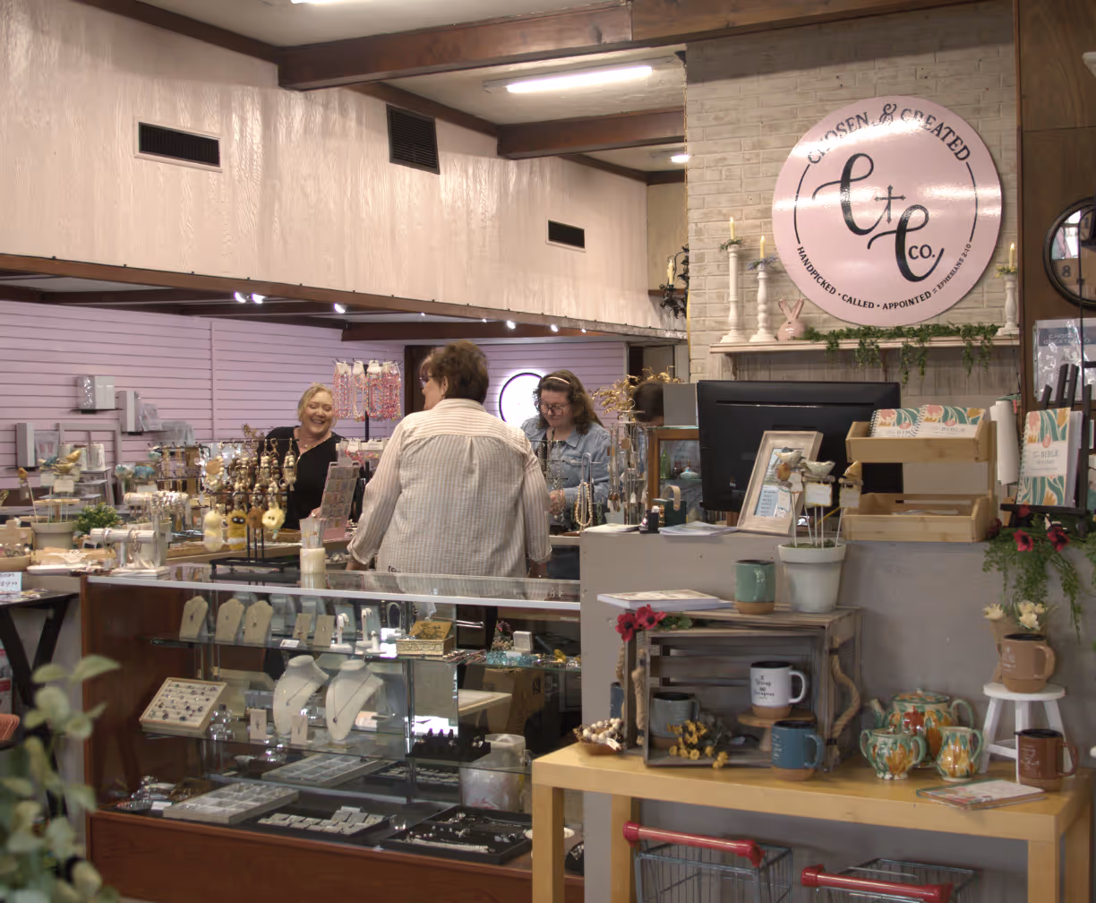Three women shopping and smiling inside a cozy jewelry and gift shop with displays and decorations.