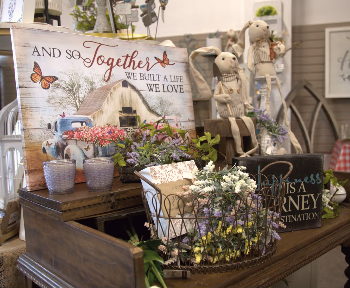 Decorative table with signs, flowers, and two stuffed bunny dolls in a cozy rustic setting.