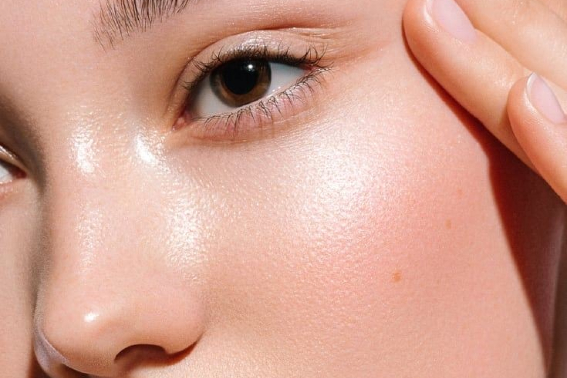 Close-up of a woman's smooth, glowing skin with brown eye and fingers touching temple.