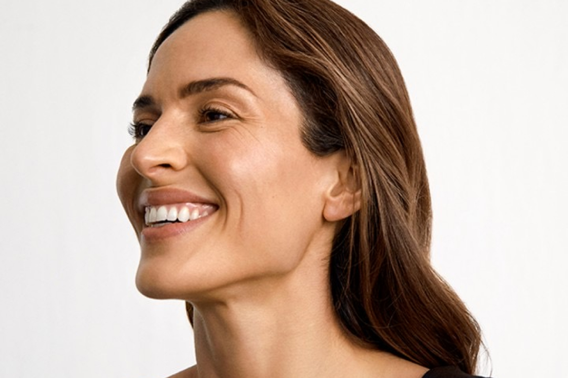 Smiling woman with long brown hair looking to the left against a plain white background.