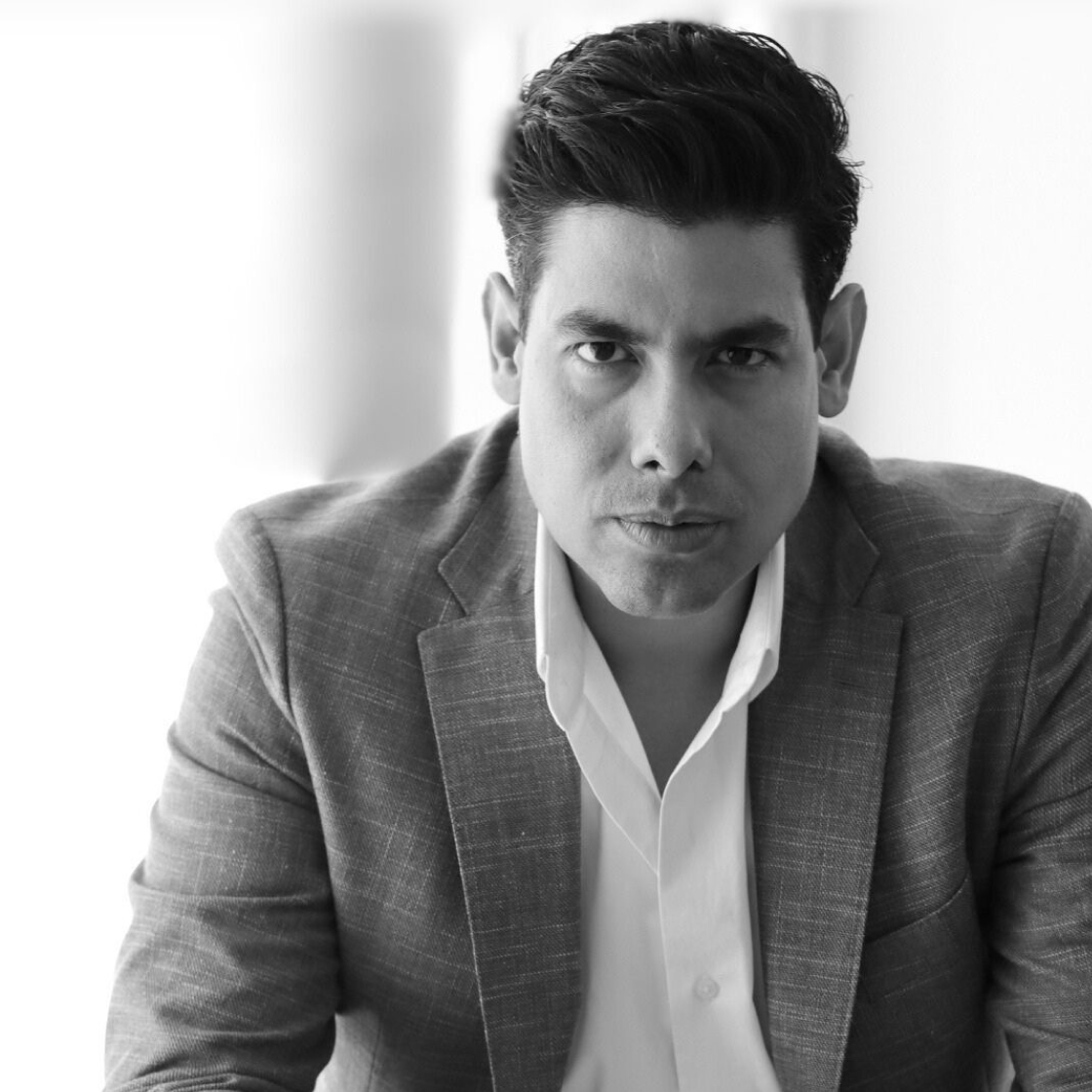 Dr. Fernando Barbosa in a suit leaning on a pool table in a modern room with plants and pendant light.