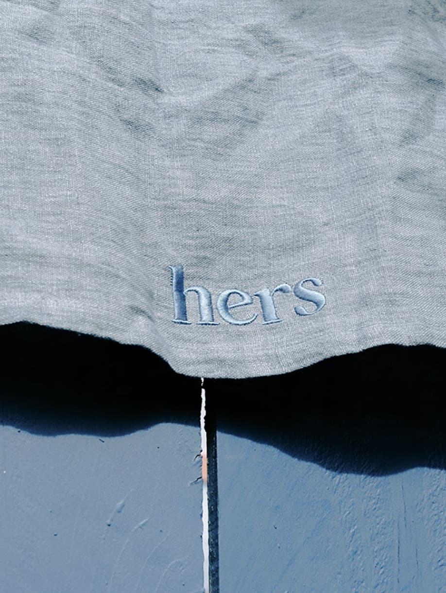 Close-up of Hers custom blue linen napkin with embroidered logo