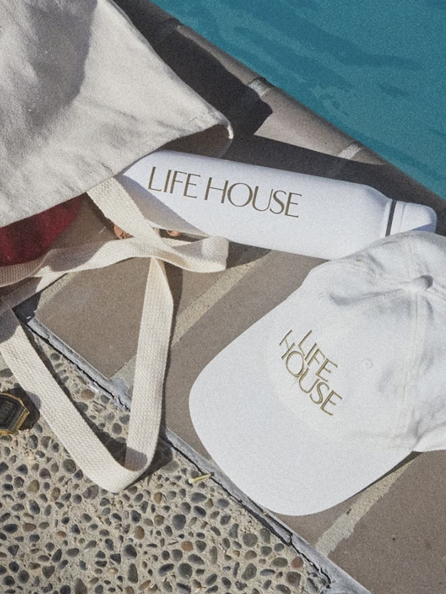 Life House custom tote bag, cap, and water bottle beside pool