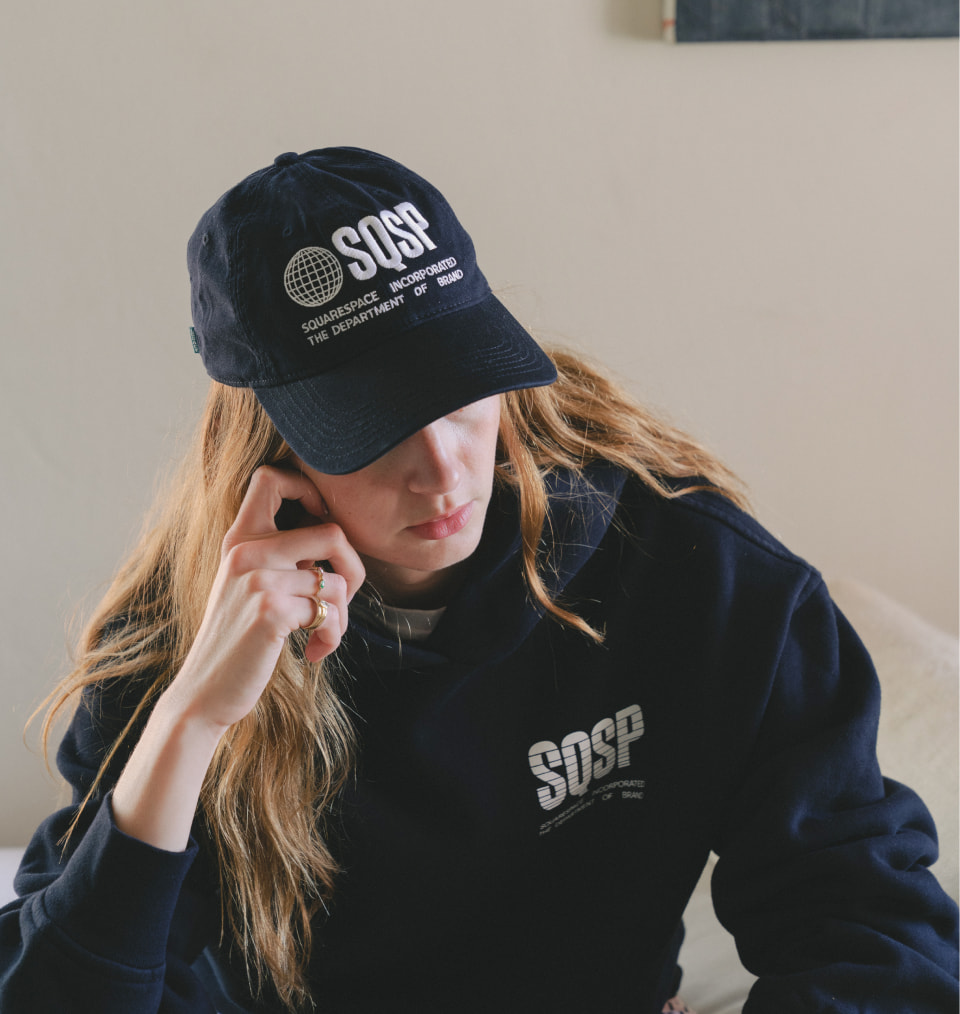 Model wearing black cap and pullover with SquareSpace embroidered in white