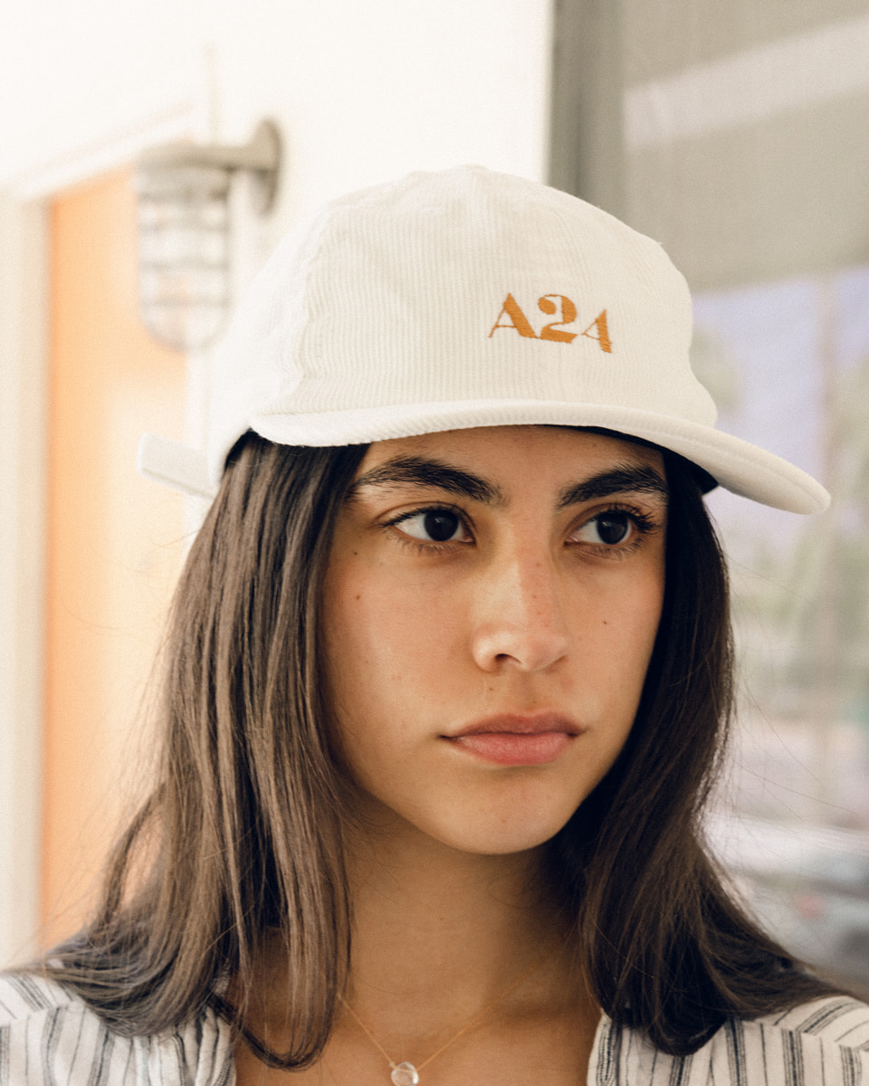 Model wearing white corduroy cap with gold A24 logo embroidery