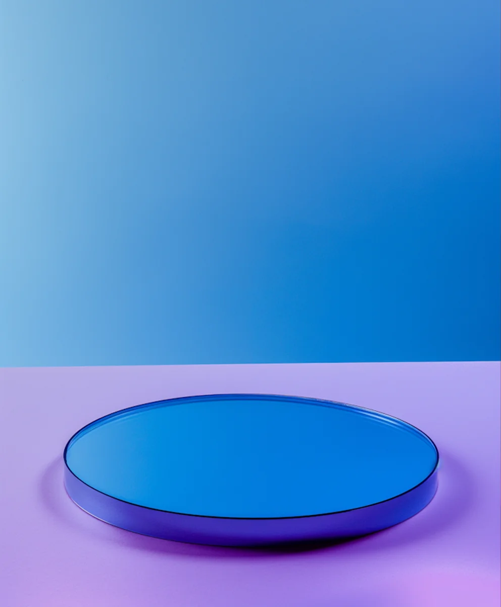 Round blue mirror-like object on a purple surface with a gradient blue background.