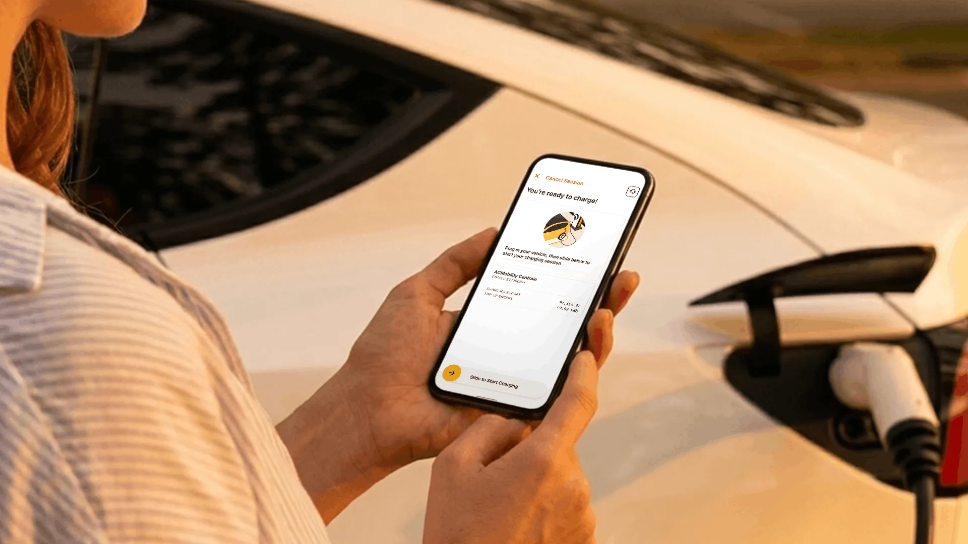 Driver holding a phone beside a plugged-in electric car.