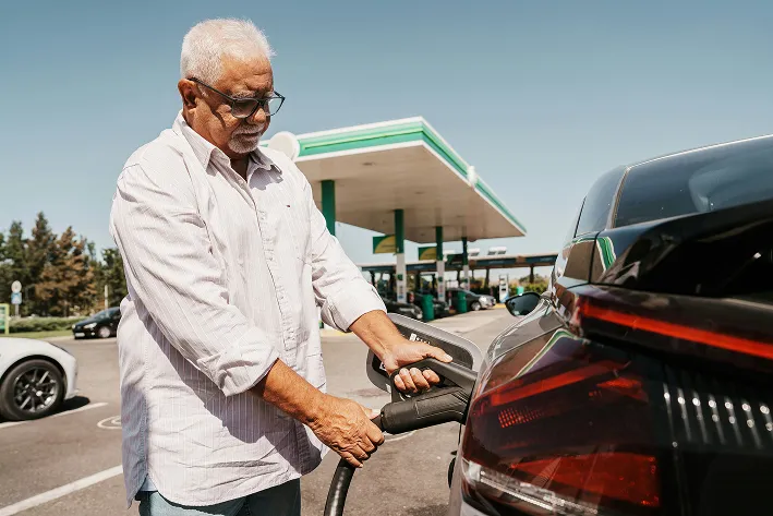Man plugging a charger into an electric vehicle at a station.
