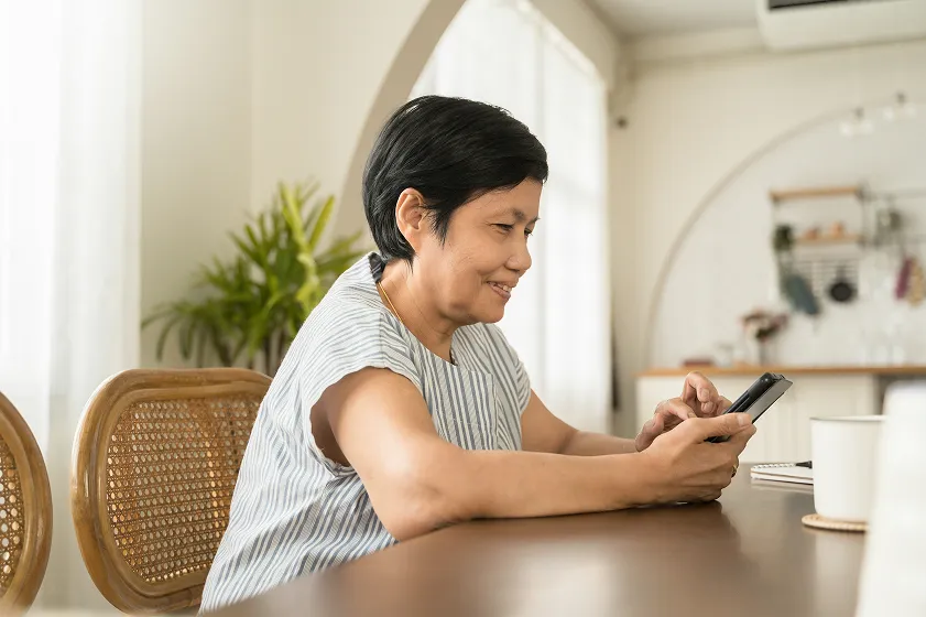 Woman smiling at a phone while seated at a table.
