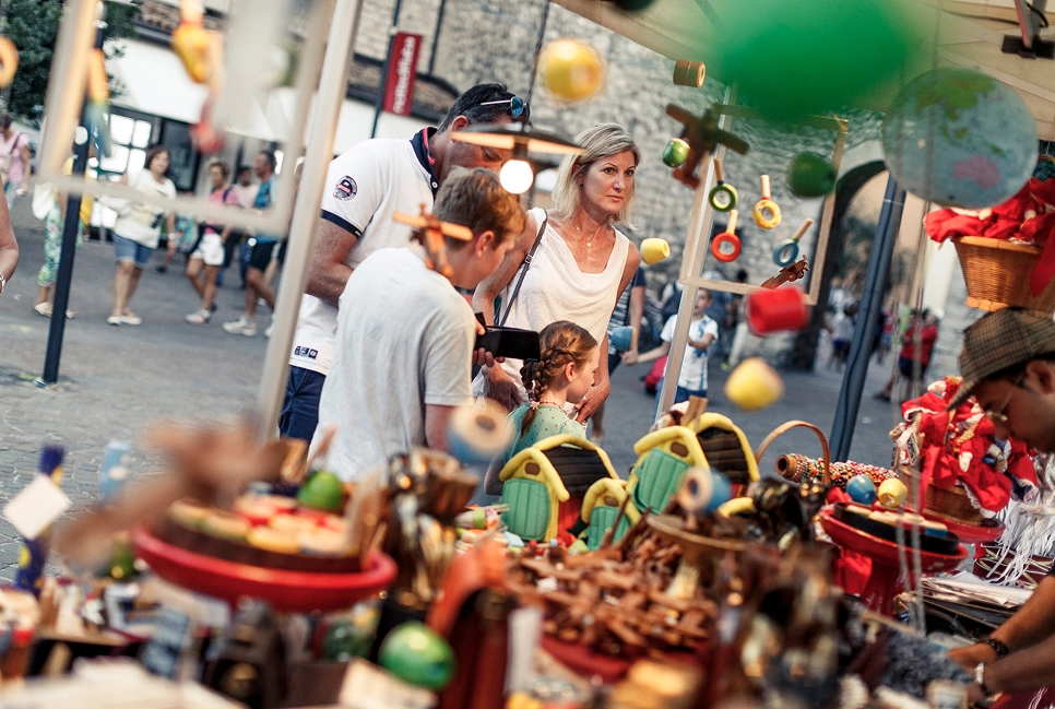 Famiglia guarda giocattoli colorati esposti a un mercato all'aperto in una via lastricata.