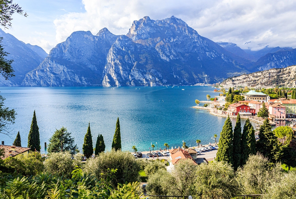 Vista panoramica del Lago di Garda con montagne, acqua blu e case colorate in riva.