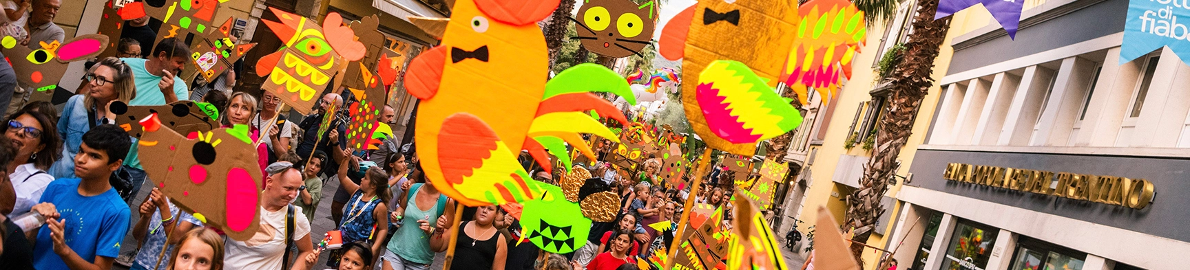 Folla in una via con pupazzi colorati fatti a mano durante una festa o parata.