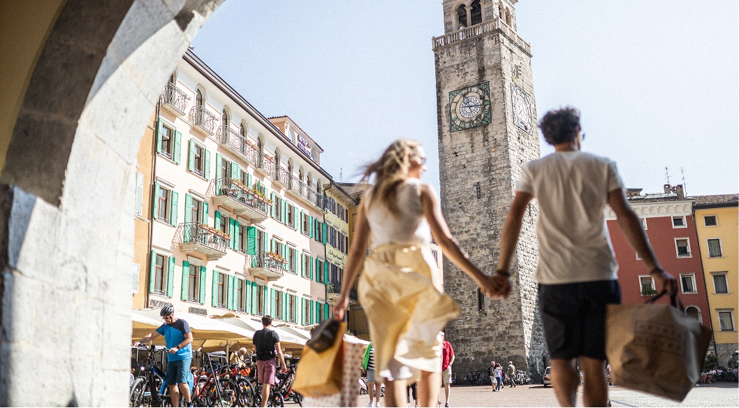 Coppia che cammina mano nella mano in una piazza con edificio storico e torre Apponale.