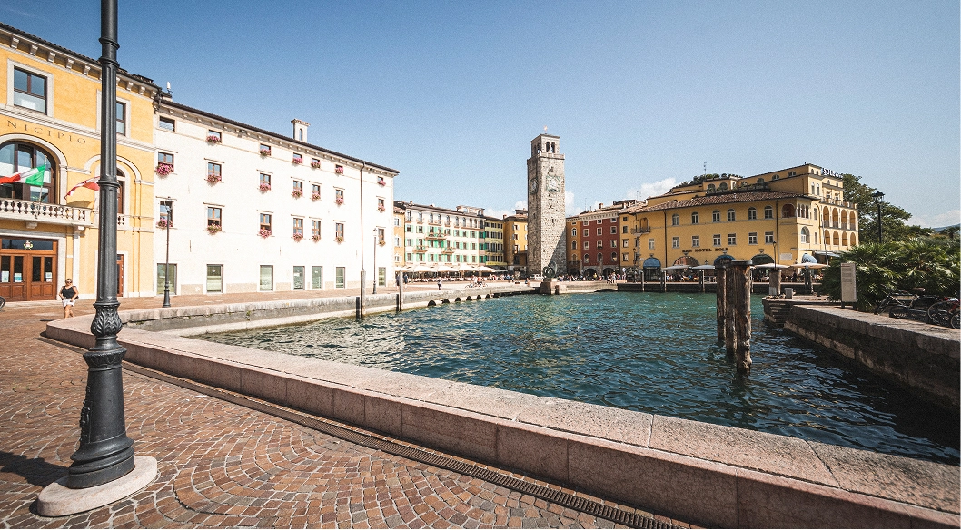 Vista del lungolago con edifici colorati e una torre Apponale sotto un cielo sereno.