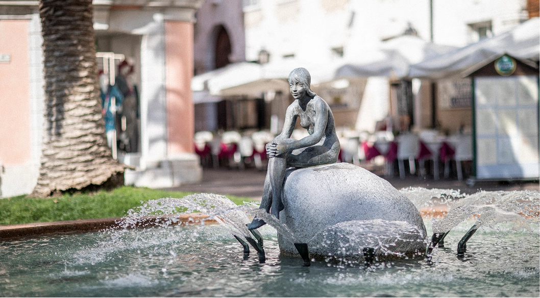Statua di una figura femminile seduta su una roccia in una fontana con acqua che spruzza.