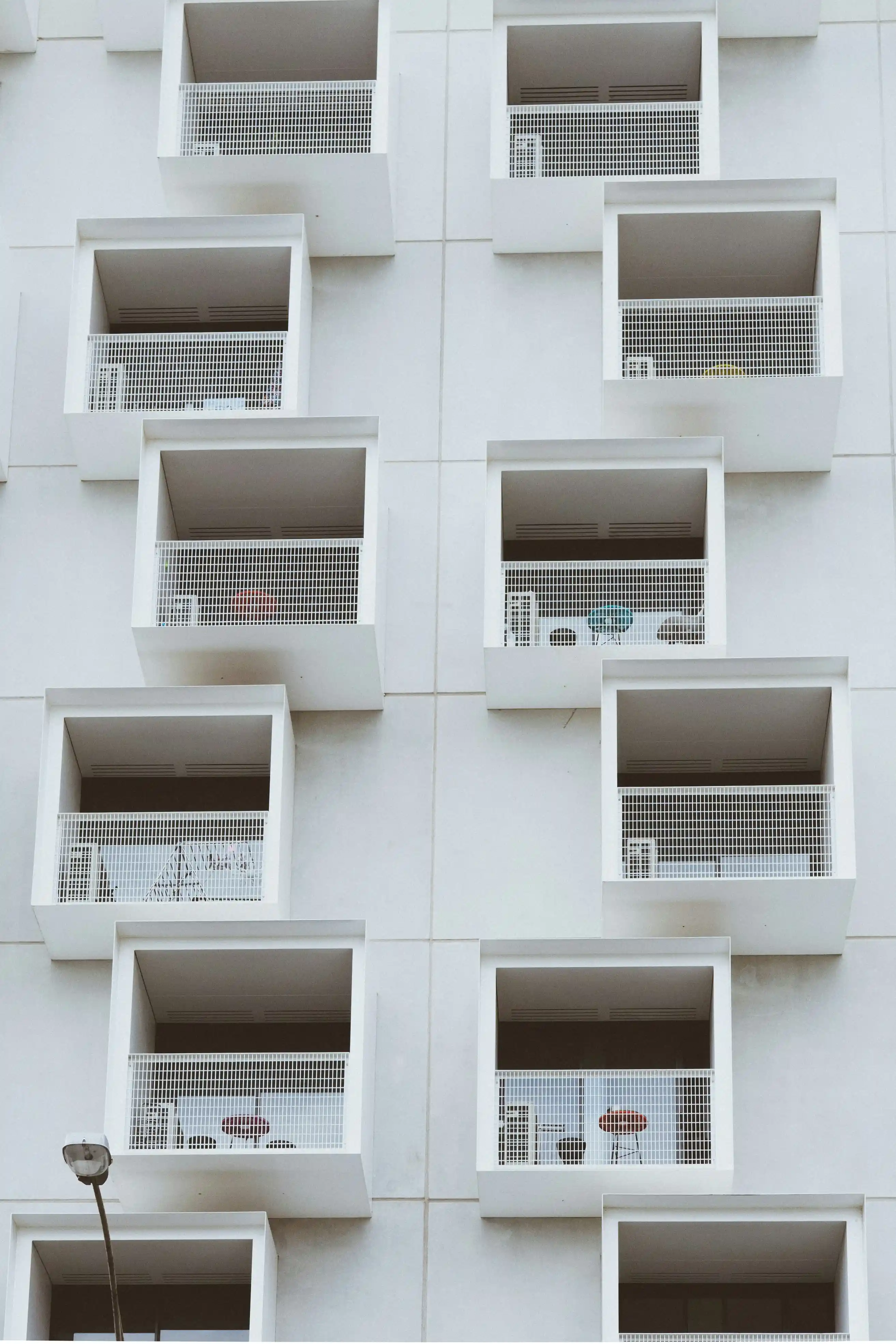 Façade d'un immeuble moderne avec plusieurs balcons carrés en saillie, protégés par des grilles blanches.