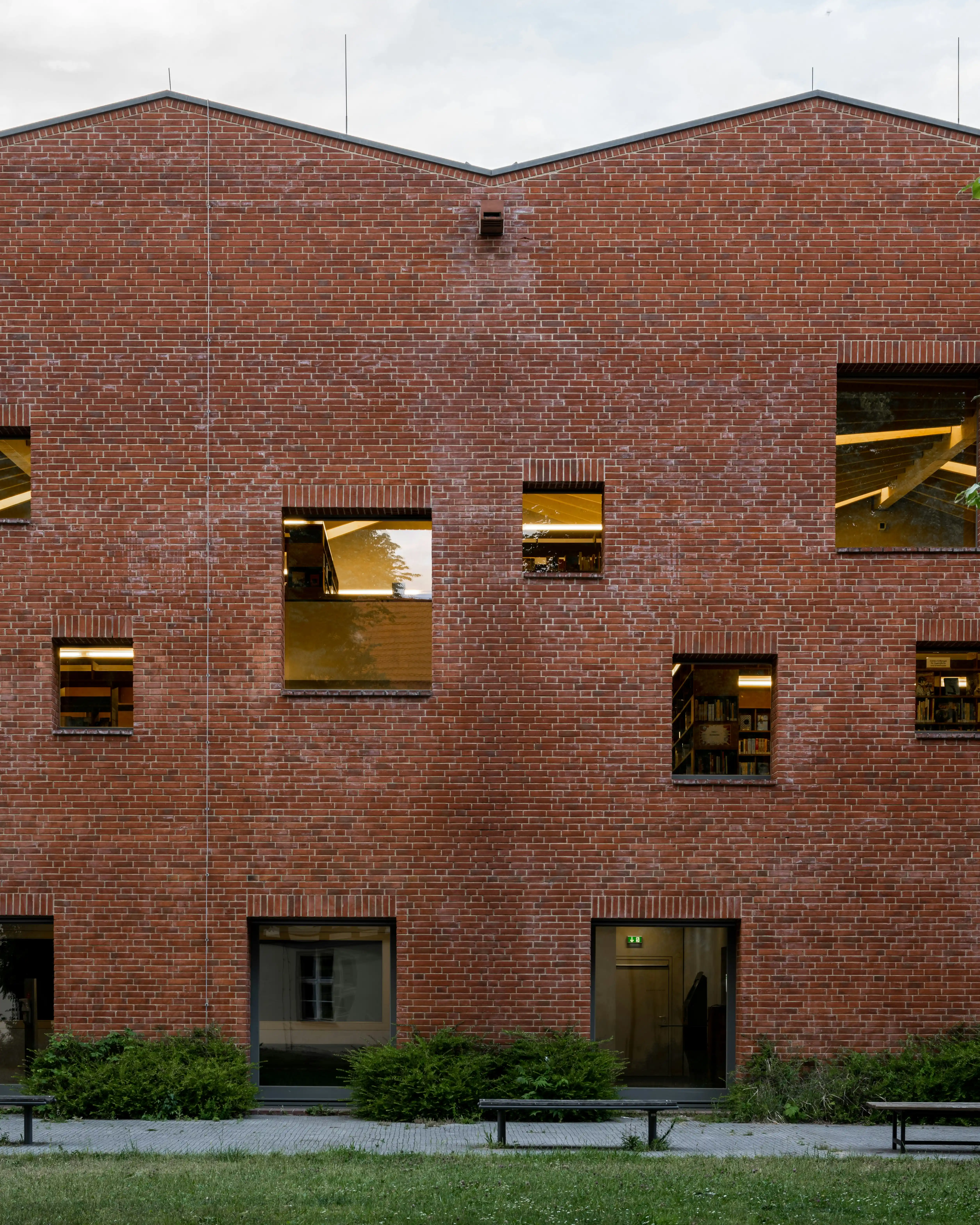 Façade en briques rouges d'un bâtiment avec plusieurs fenêtres de tailles variées et un espace vert devant.