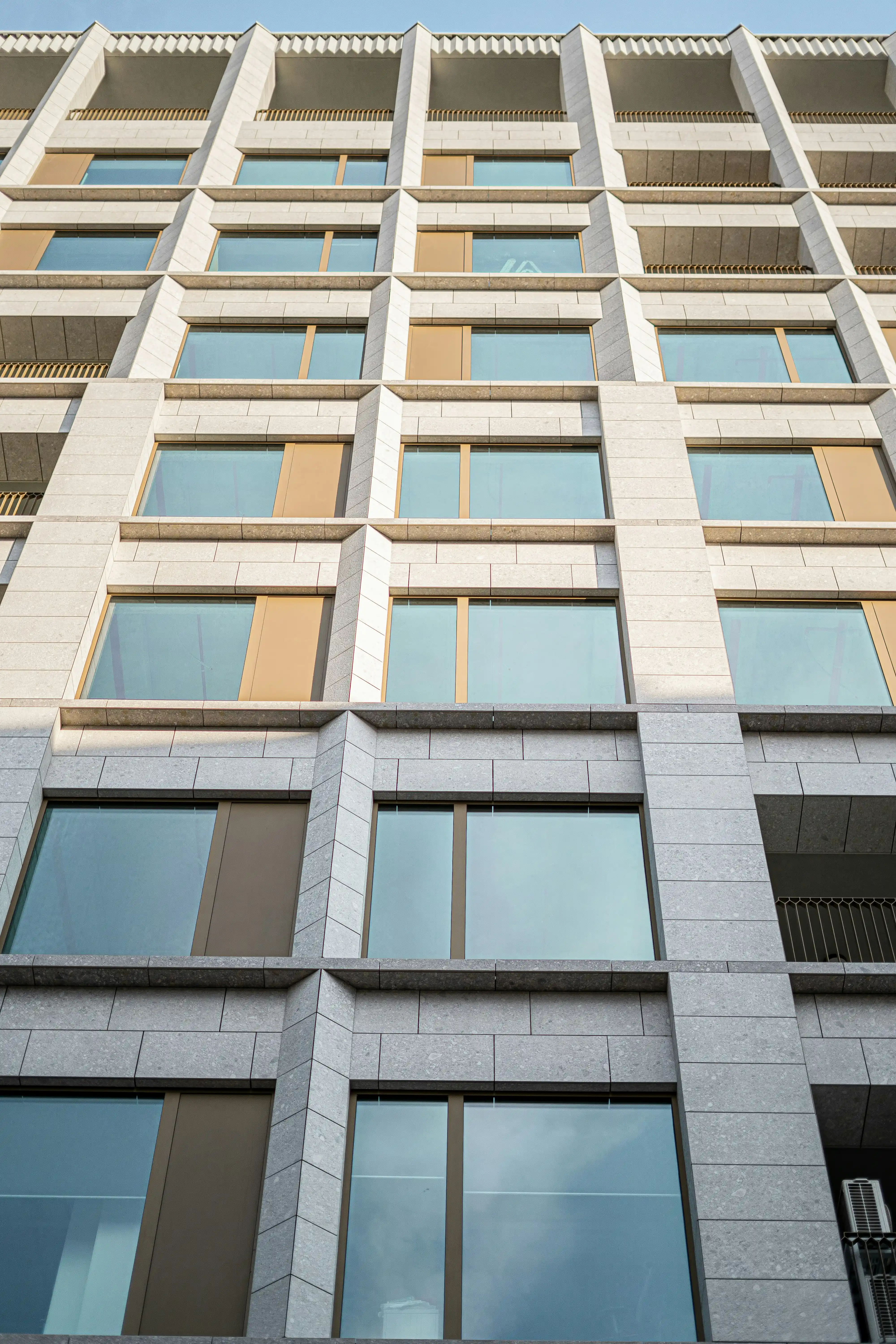 Façade d'un immeuble moderne avec grandes fenêtres rectangulaires encadrées de pierre claire.