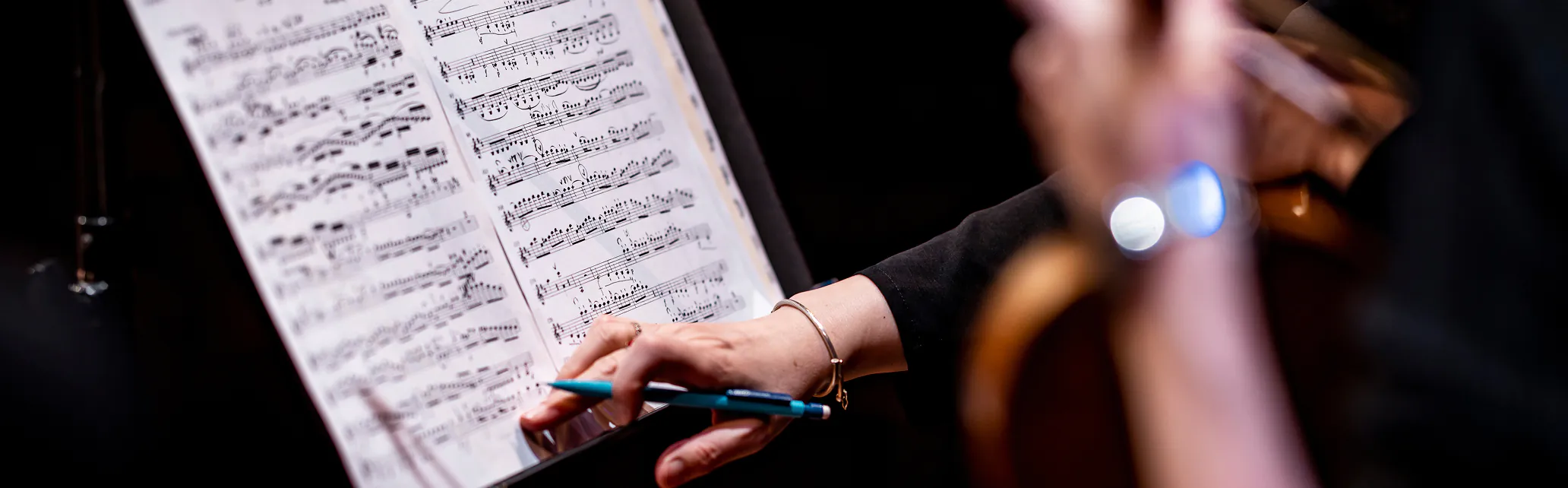 Musician reading sheet music while holding a pen and playing a string instrument.
