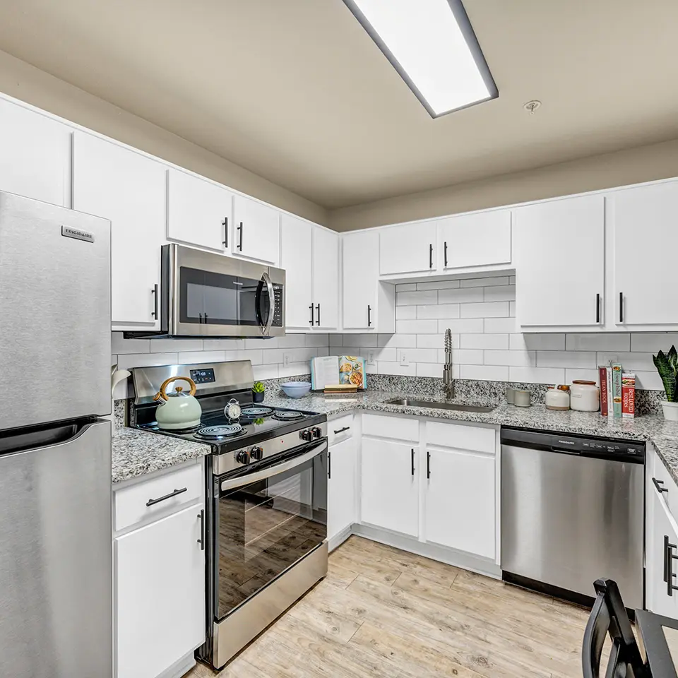 Modern kitchen with white cabinets, stainless steel appliances including refrigerator, stove, microwave, and dishwasher, granite countertops, and wood flooring.