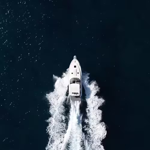 A white boat creating a wake as it moves through dark blue water, viewed from above.