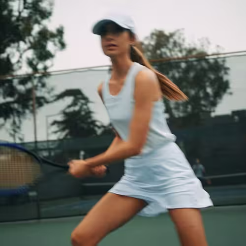 Woman in white sportswear and cap playing tennis on an outdoor court.