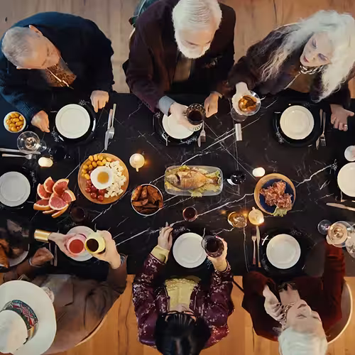 Top view of six people sitting around a table sharing a meal with various dishes and drinks.