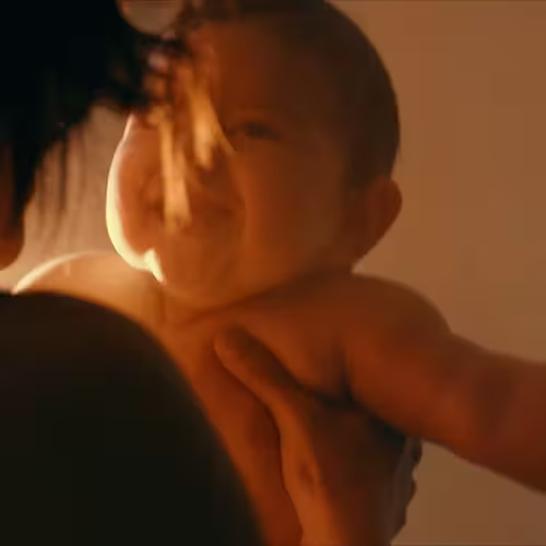 Adult holding and smiling at a laughing baby in warm soft lighting.