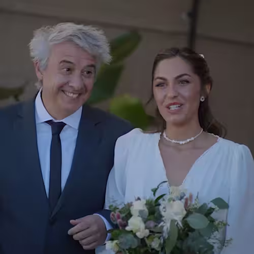 Woman in white dress holding bouquet standing next to smiling man in suit and tie outdoors.
