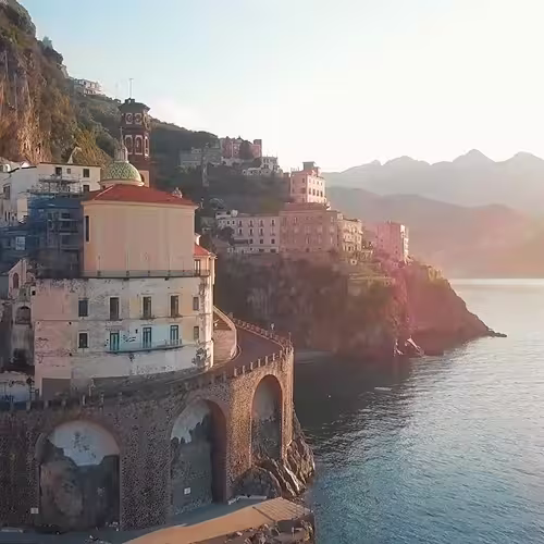 Coastal town with buildings on cliffs overlooking calm sea during sunset or sunrise.