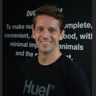 Smiling man wearing a black Huel shirt standing in front of a blurred text background.