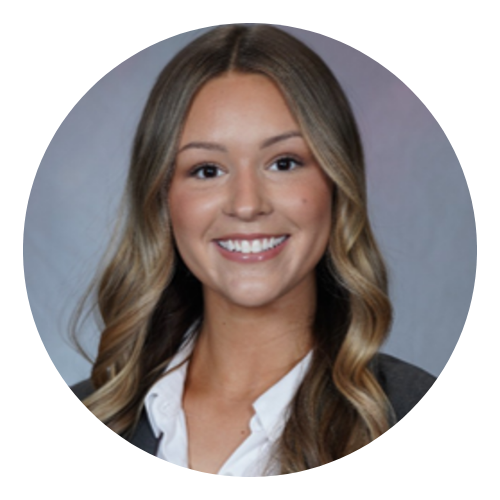 Smiling young woman with long wavy hair wearing a white shirt and dark blazer on gray background.