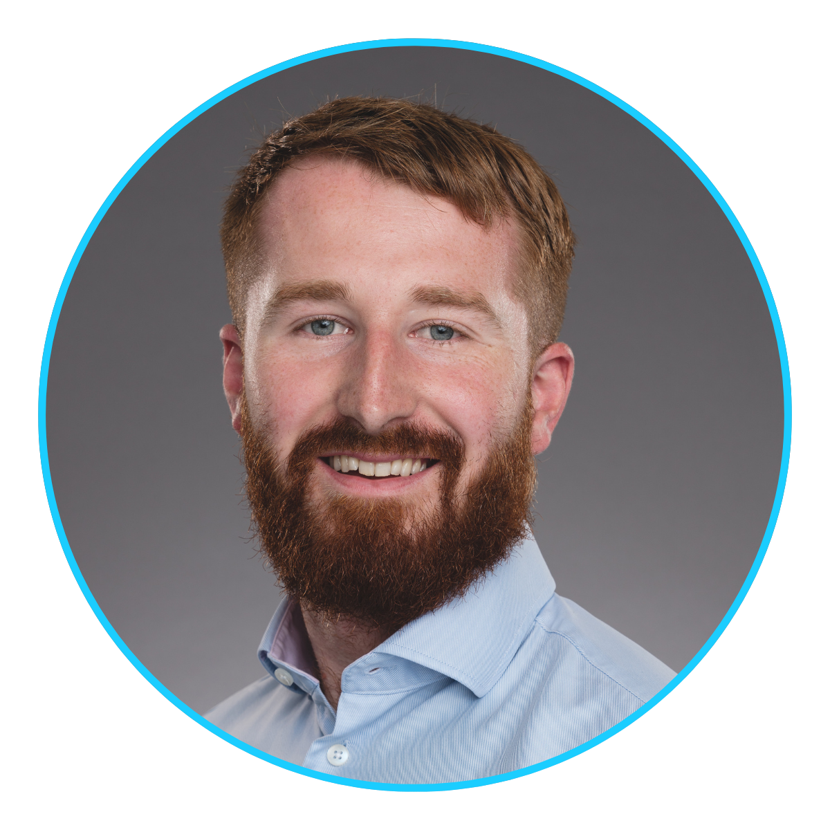 Smiling man with red beard and blue eyes, wearing a light blue collared shirt against a gray background.