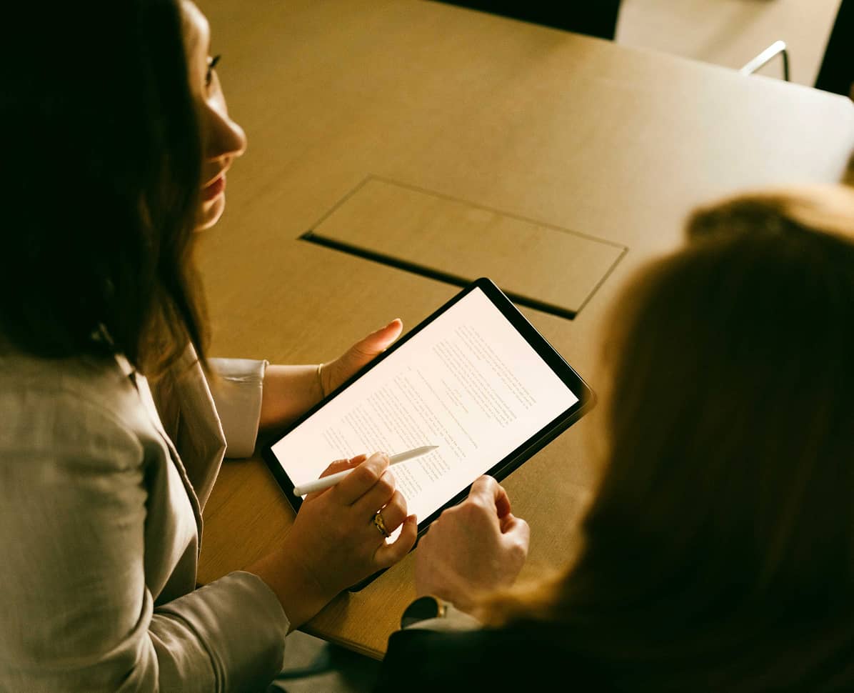 Two people at a table reviewing a document on a tablet with a stylus pen.
