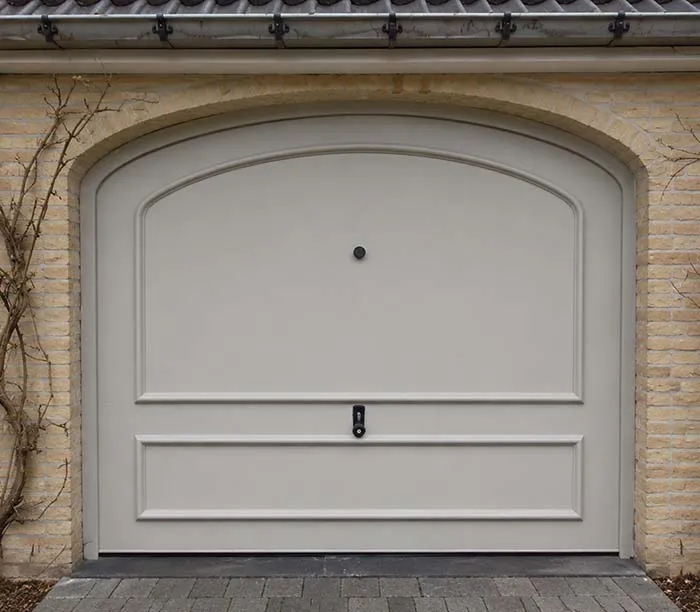 Porte de garage beige avec poignée noire encadrée de briques jaunes et pavés gris devant.