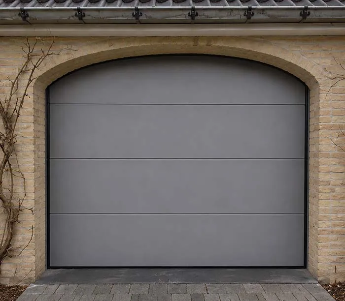 Porte de garage grise moderne avec cadre en briques jaunes et portail voûté.