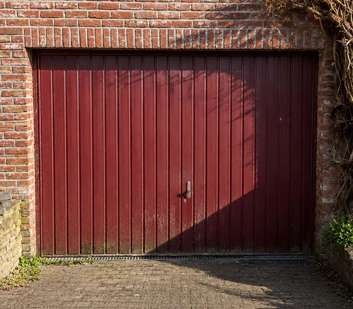 Porte de garage en bois rouge avec poignée, encadrée par un mur en briques rouges.