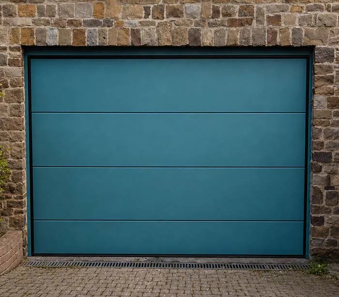 Porte de garage bleue à panneaux horizontaux encadrée de pierre avec pavés autour.