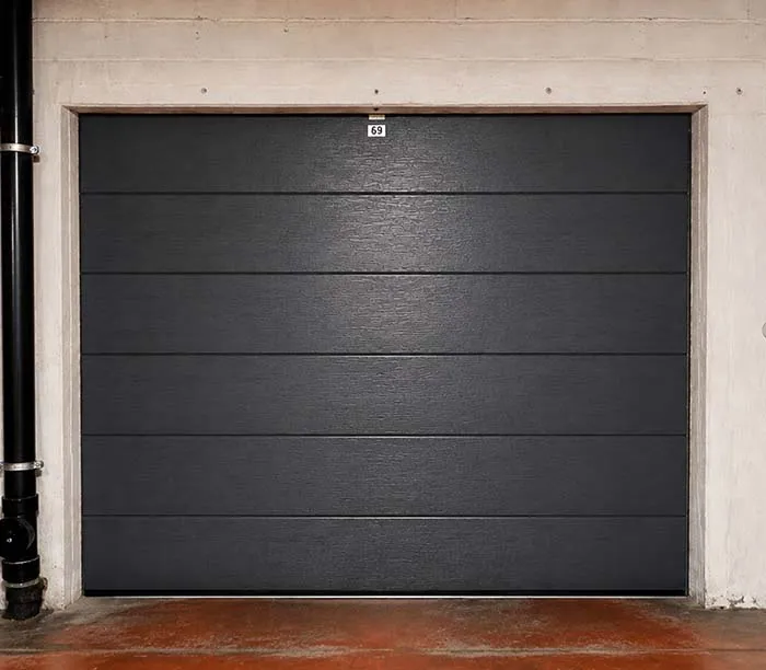 Porte de garage noire avec le numéro 69 au-dessus encadrée de murs blancs.