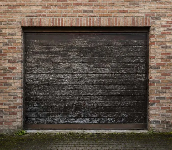 Porte de garage noire horizontale avec des taches et encadrement en briques rouges.