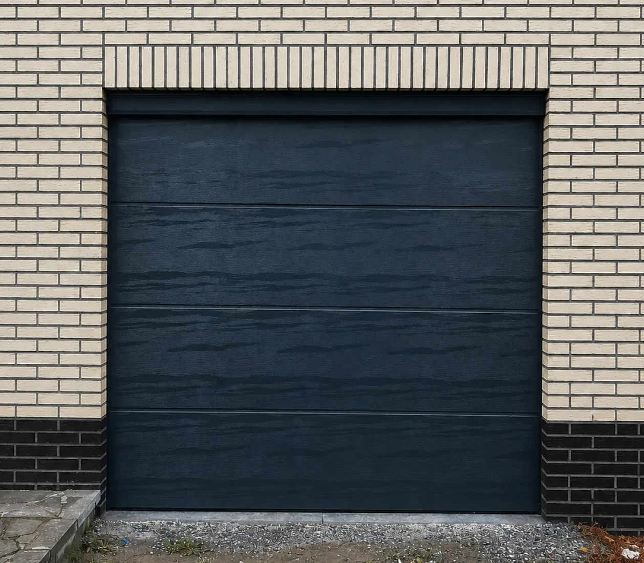 Porte de garage noire moderne encadrée par un mur en briques claires et sombres.
